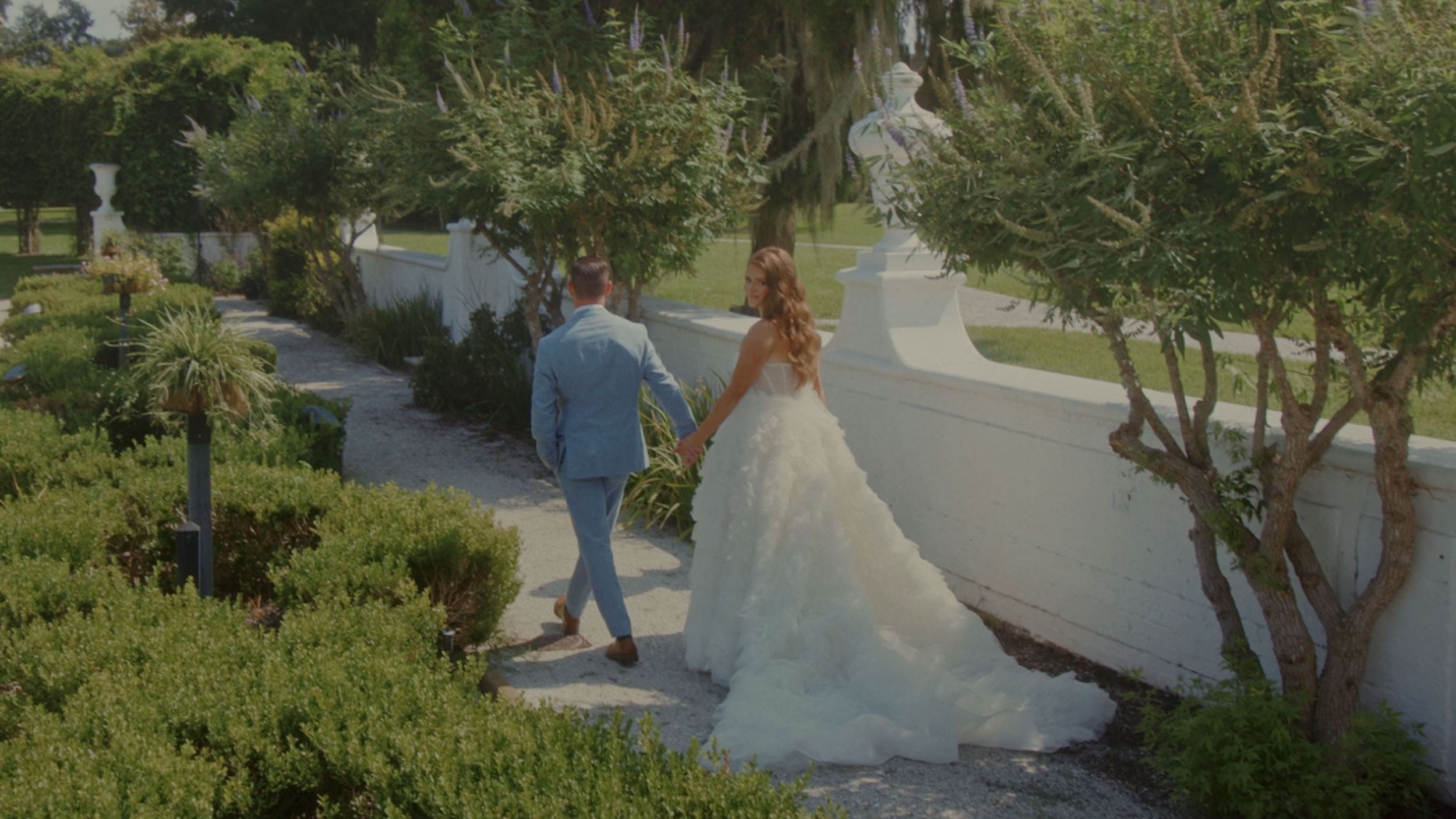 man in blue suite leading women in wedding dress down a walkway in a garden