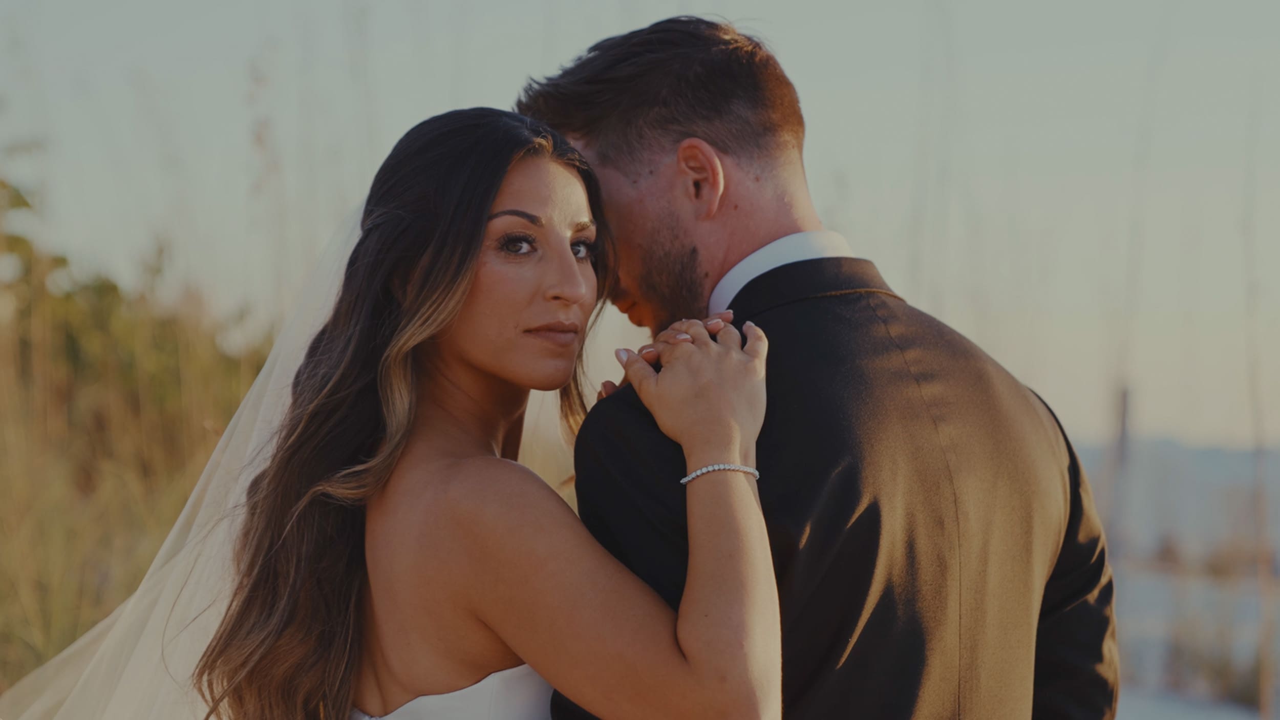 women in wedding dress with her arm on husbands shoulder looking towards camera